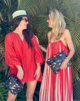 Two women in red outfits standing in front of tropical plants, holding butterfly-patterned bags.
