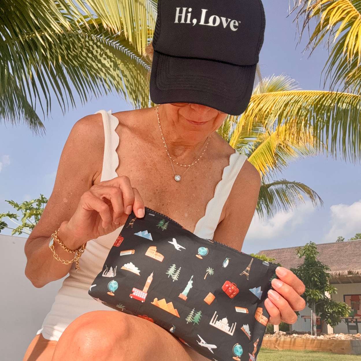 Person holding a black pouch with colorful  travel patterns against a palm tree background