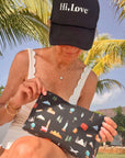 Person holding a black pouch with colorful  travel patterns against a palm tree background