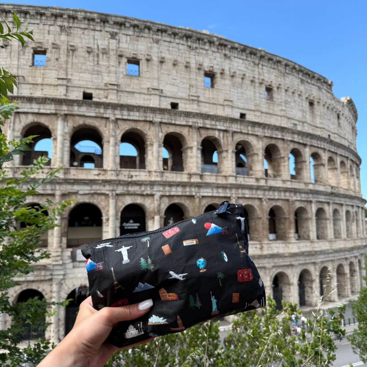Black pouch with colorful landmark designs held in front of the Colosseum in Rome.