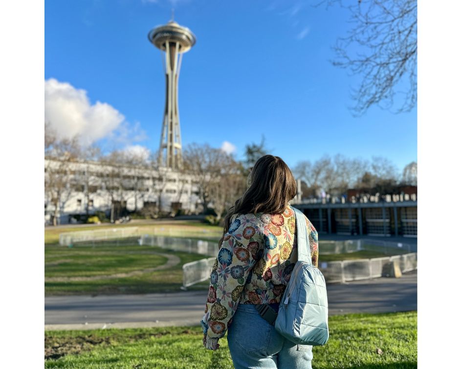 Woman in floral jacket and blue puffer crossbody backpack looking at the space needle