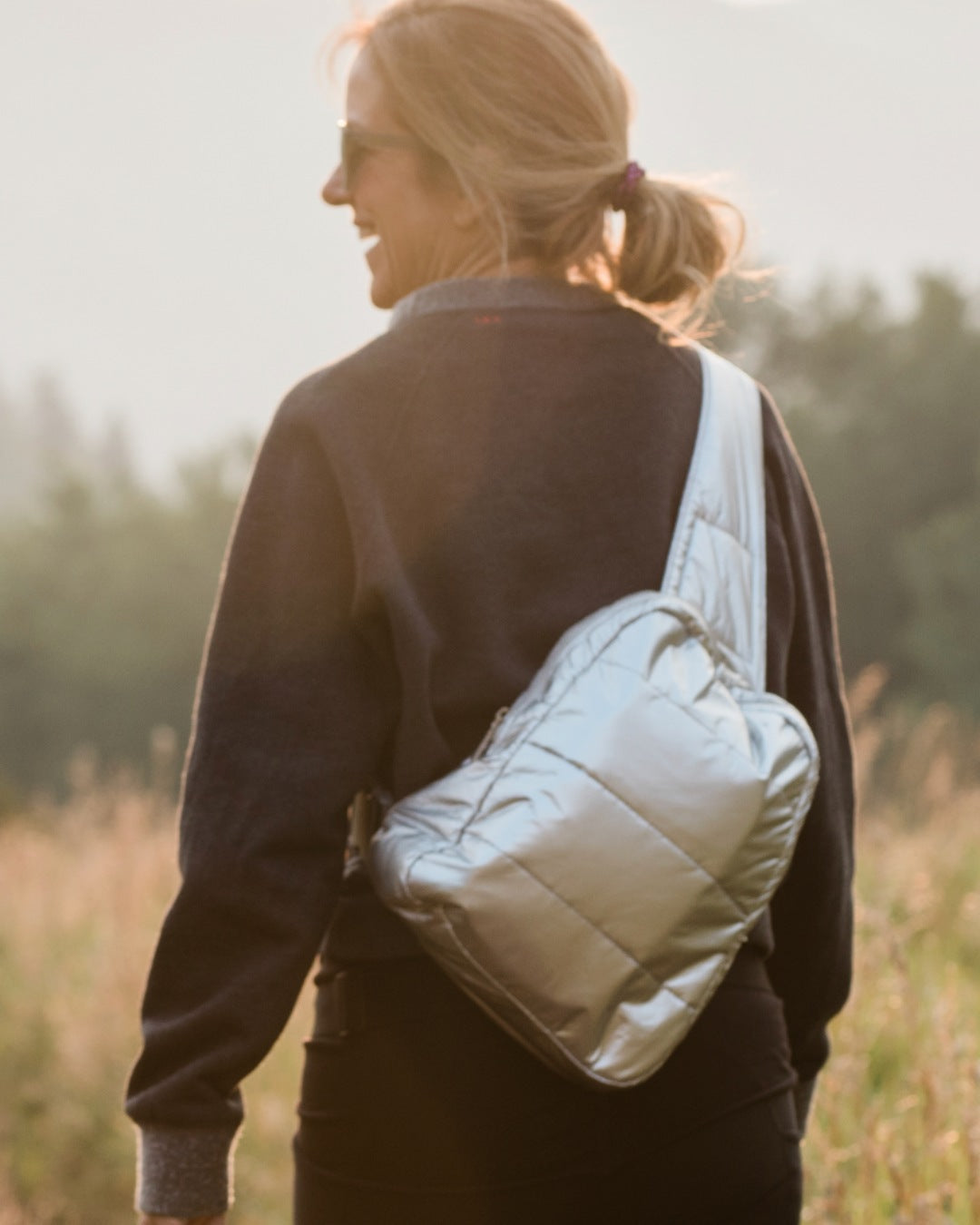 Woman in field wearing silver crossbody backpack