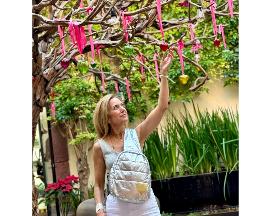 Woman wearing crossbody backpack looking at glass blown hearts on a tree