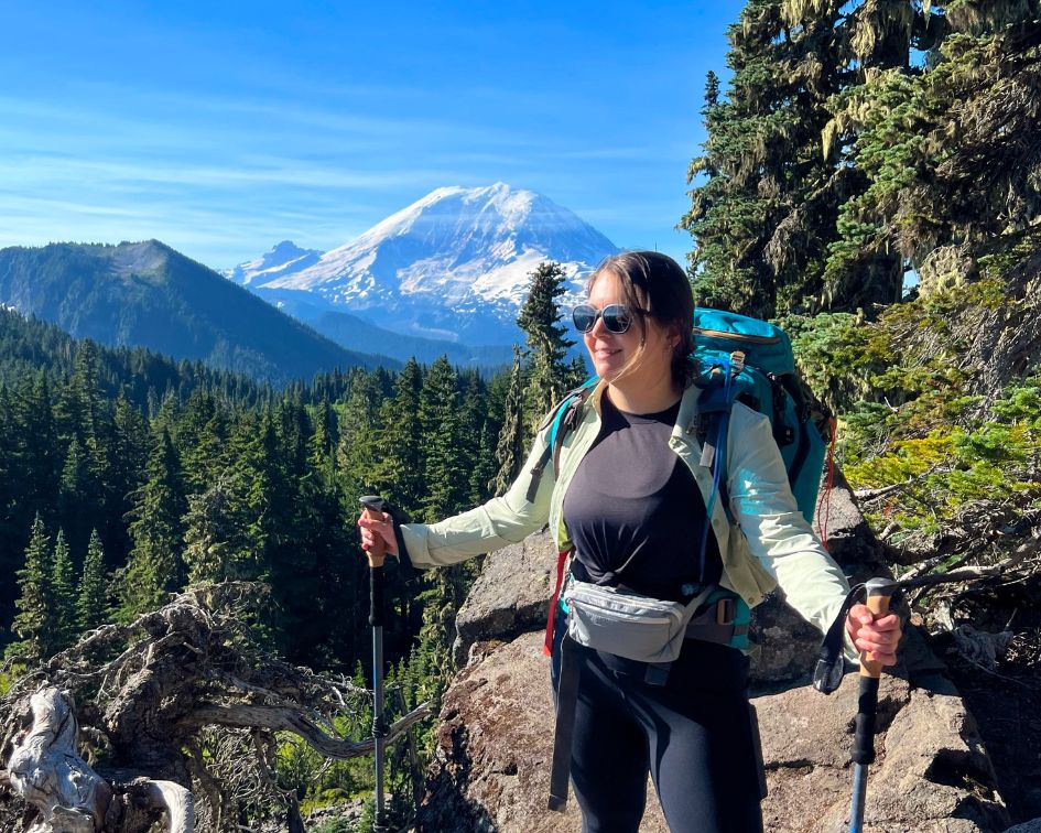 Woman hiking in Mount Rainier National Park carrying hiking poles, wearing backpack and puffer fanny pack belt bag in gray