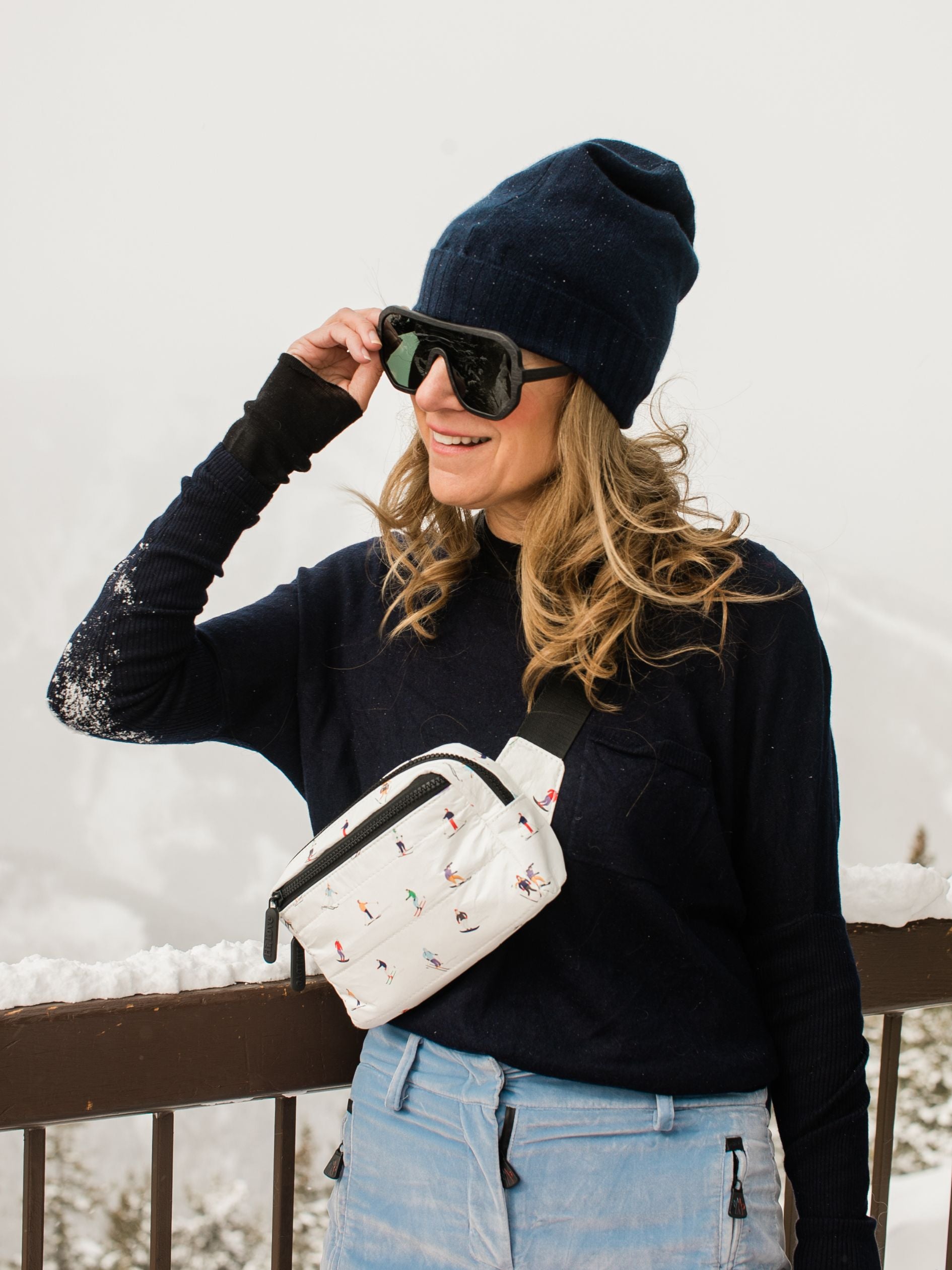 Woman outside in snow wearing puffer crossbody fanny pack belt bag in dancing skiers