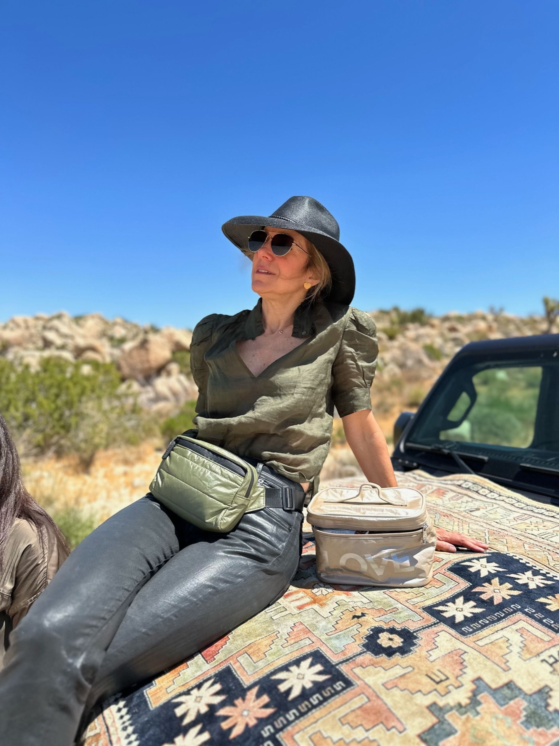 Woman in desert sitting on car wearing Puffer Crossbody Fanny Pack Belt Bag in Shimmer Olive Green