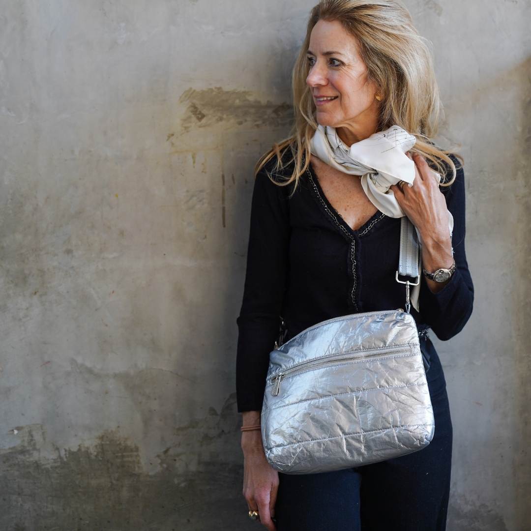 Woman wearing a silver crossbody puffer handbag against a textured wall.