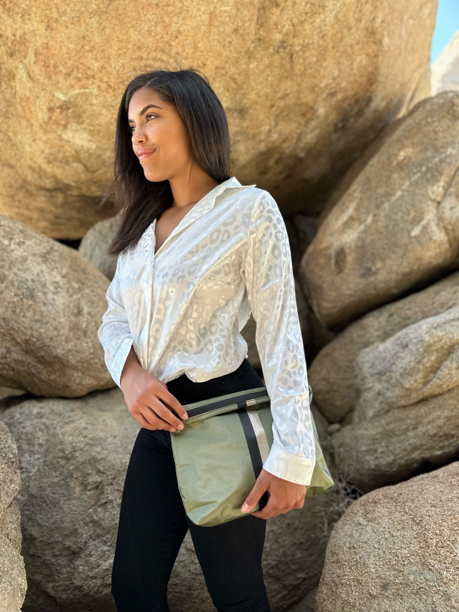 Woman standing in front of large rocks holding a shimmer green clutch purse