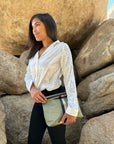 Woman standing in front of large rocks holding a shimmer green clutch purse