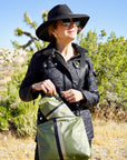 Woman in black jacket and hat wearing a shimmer green crossbody purse