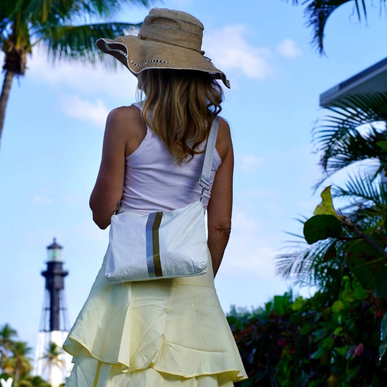 Woman standing wearing sunhat and white crossbody purse with blue sky and palm trees
