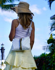 Woman standing wearing sunhat and white crossbody purse with blue sky and palm trees