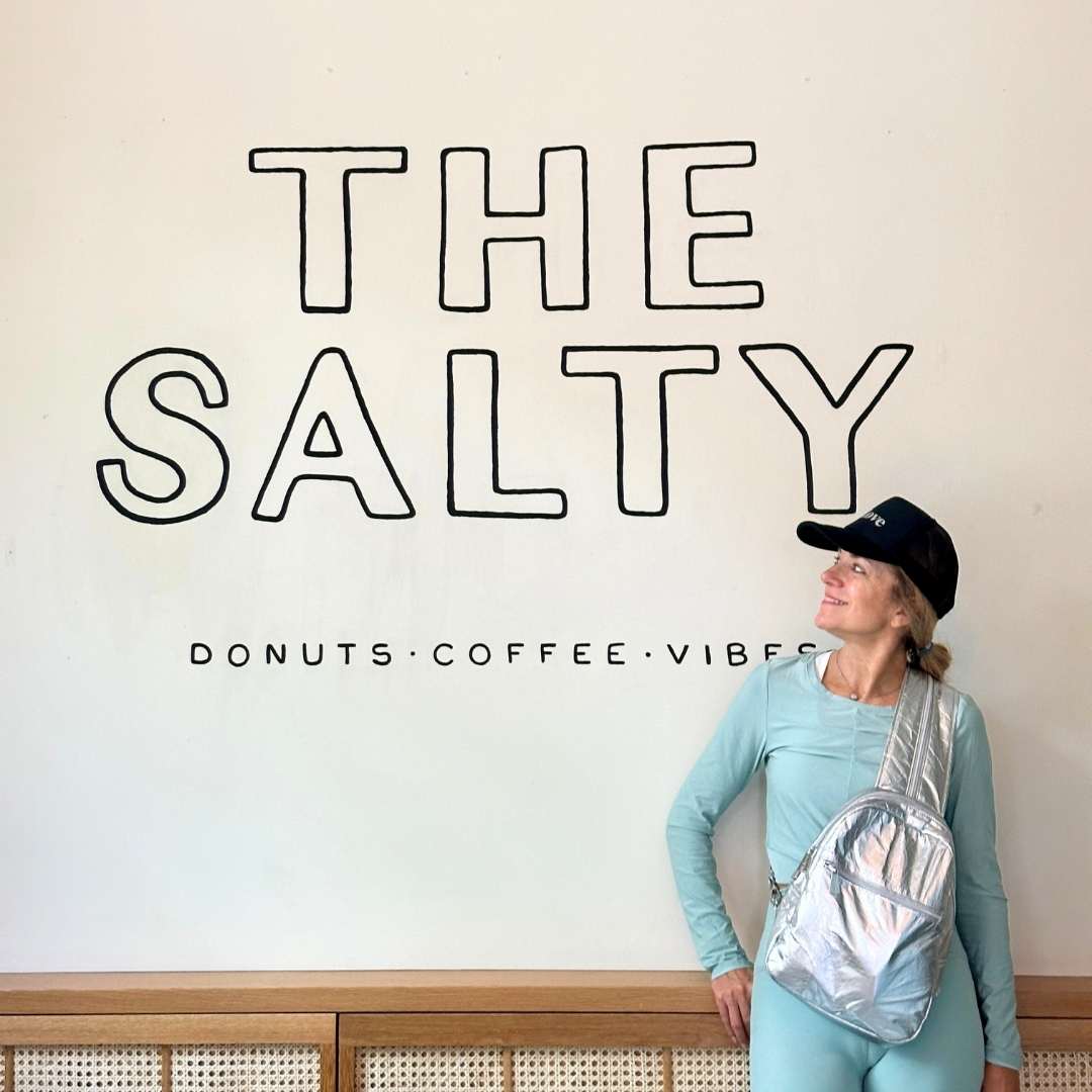 Person with a silver crossbody backpack & sling bag standing in front of 'The Salty' sign.