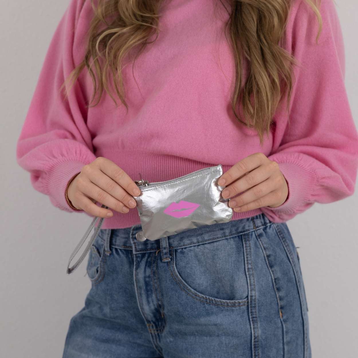 Person holding silver gift card pouch with pink lips on plain background