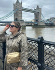 Woman standing in front of bridge in Ireland wearing gold mini puffer chain purse
