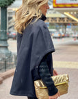 Women dressed in black carrying a gold fold over clutch handbag