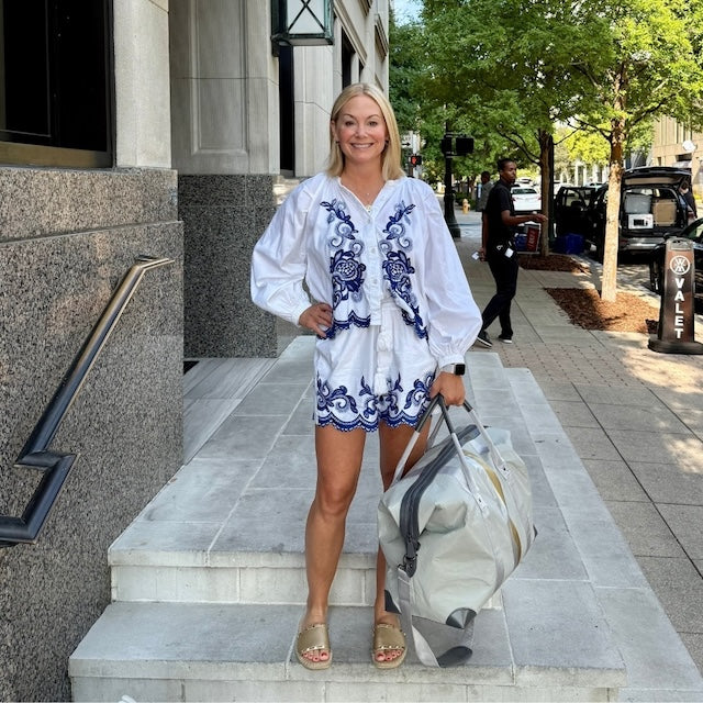 Woman in a white and blue outfit with a gray weekender bag, standing on steps outside a building.