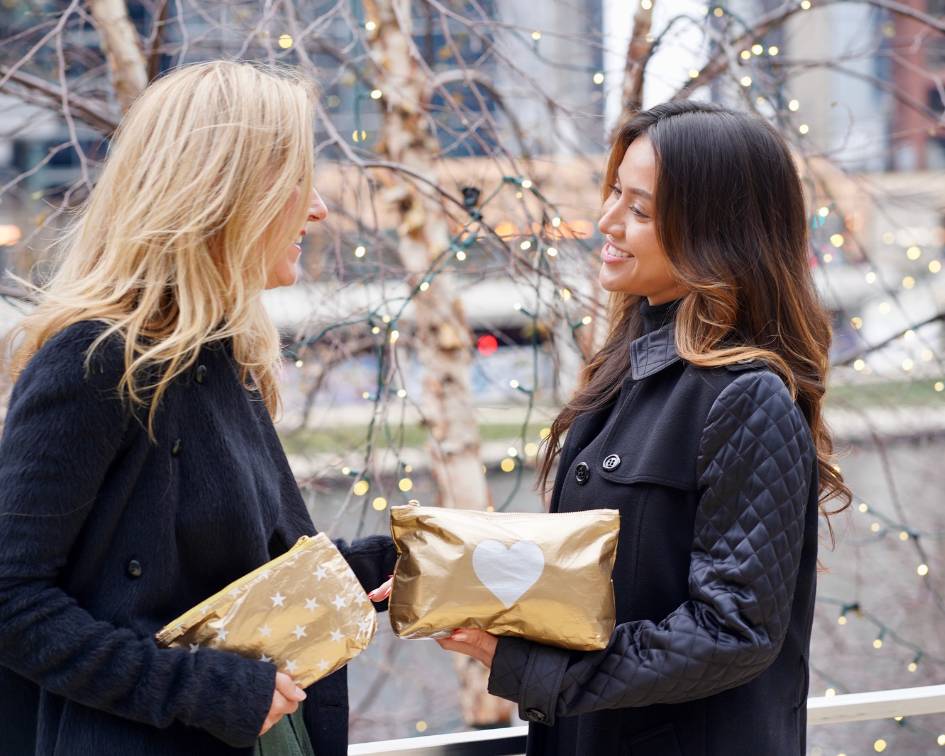 Two women talking and golding gold zipper pouches