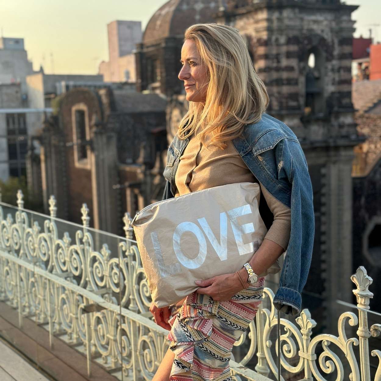 Woman holding a pouch with 'LOVE' on it, standing on a rooftop with cityscape in the background