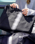 Black jumbo zipper pouch with silver and pewter center stripes styled above a matching duffle bag.