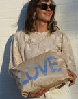 Person holding a beige bag with 'LOVE' printed on it against a white brick wall.