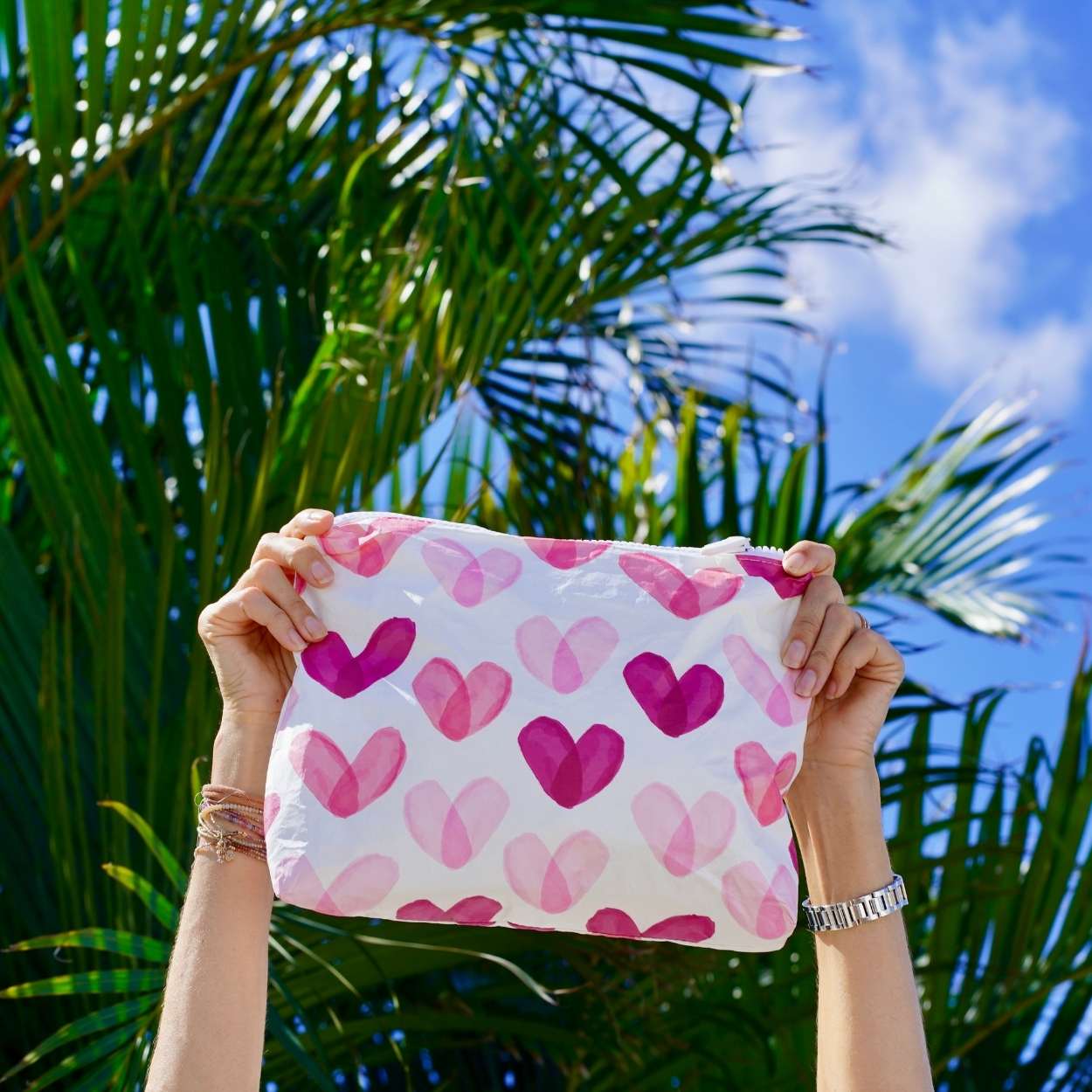 Person holding a pouch with pink heart pattern against a palm tree background