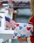 Person holding a pouch with heart patterns by a waterfront with American flags.