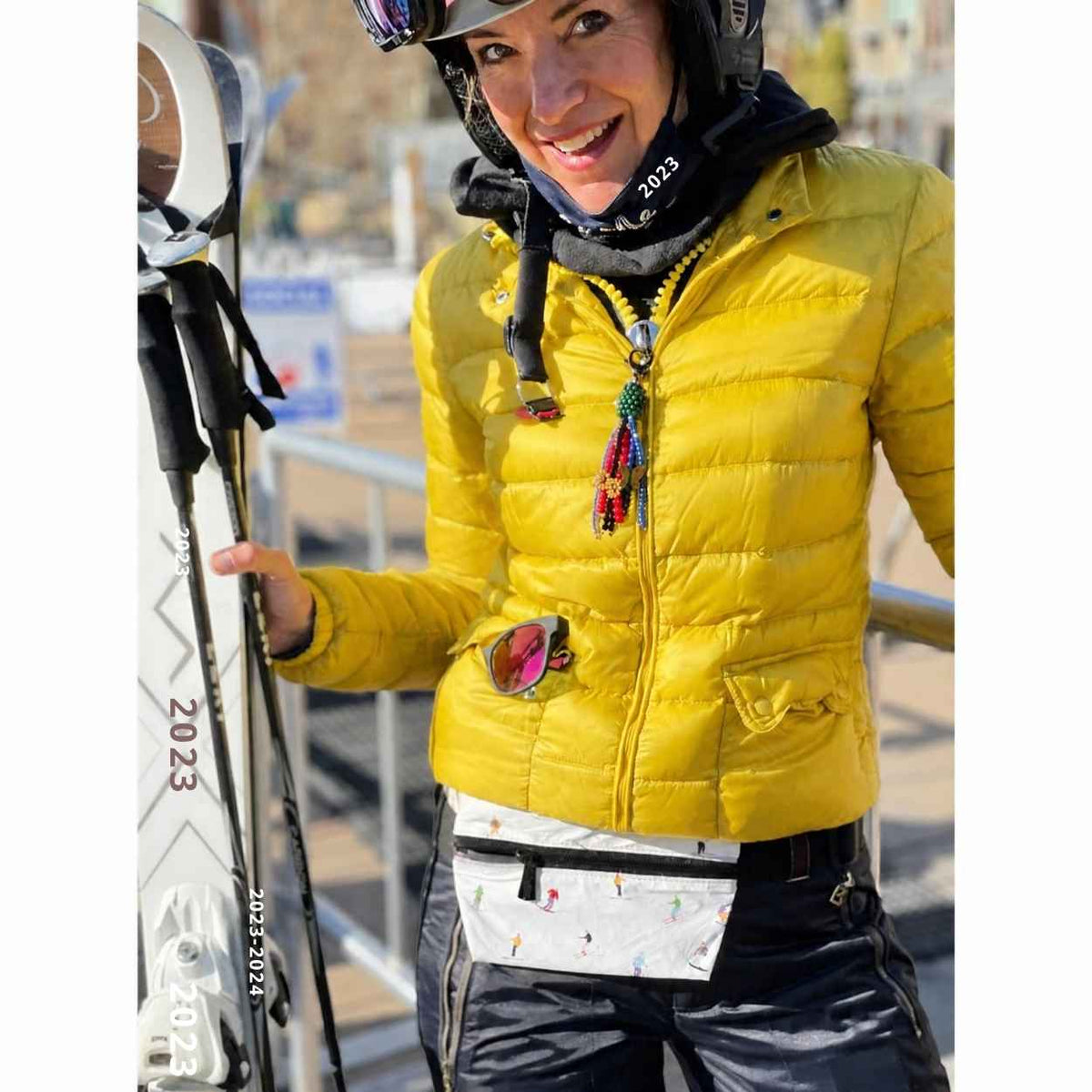 Woman outdoors with ski gear in yellow jacket wearing belt bag with skier pattern.