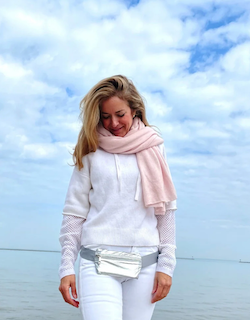 Woman wearing a white sweater and pink scarf with a fanny pack against a blue sky.