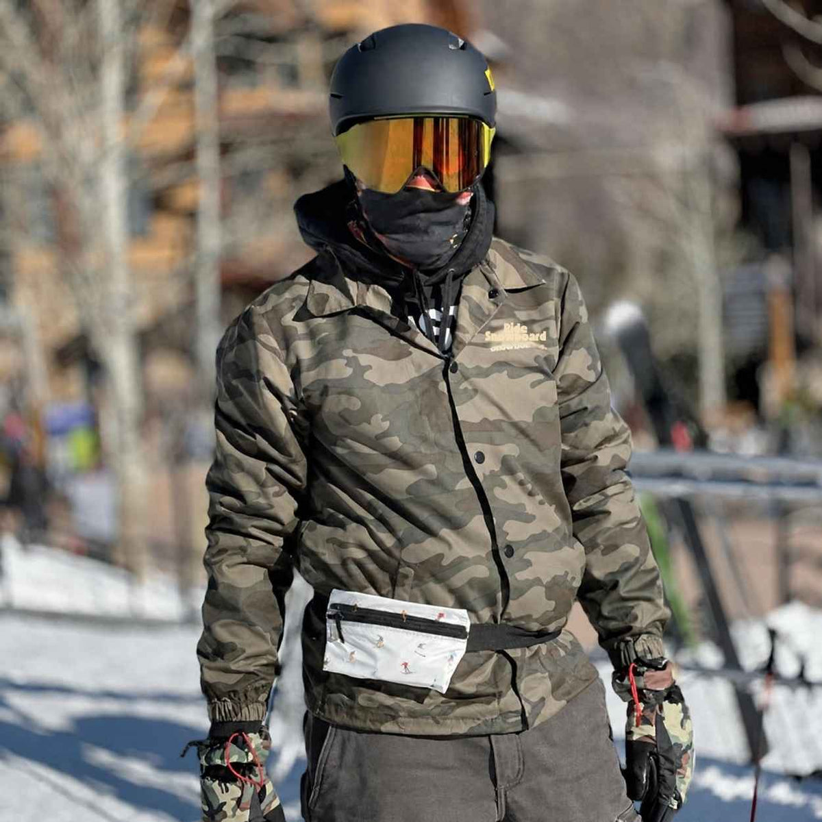 Man outdoors in ski gear wearing camo coat and fanny pack with ski inspired print.