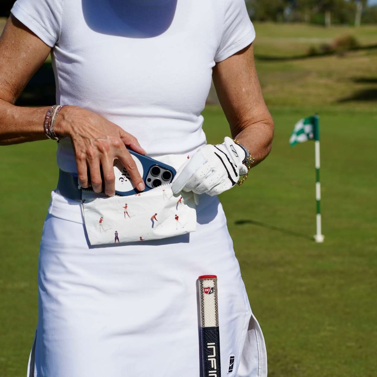 Person on a golf course holding a golf club and a fanny pack with golf-themed designs.