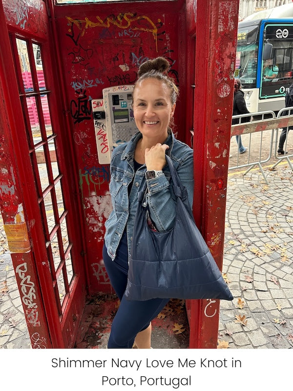Woman standing in red phone booth holding navy blue tote bag