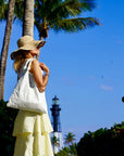 Woman wearing yellow skirt and sunhat carrying white tote bag