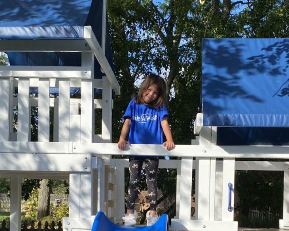 Child standing on a white playset with blue canopies in an outdoor setting