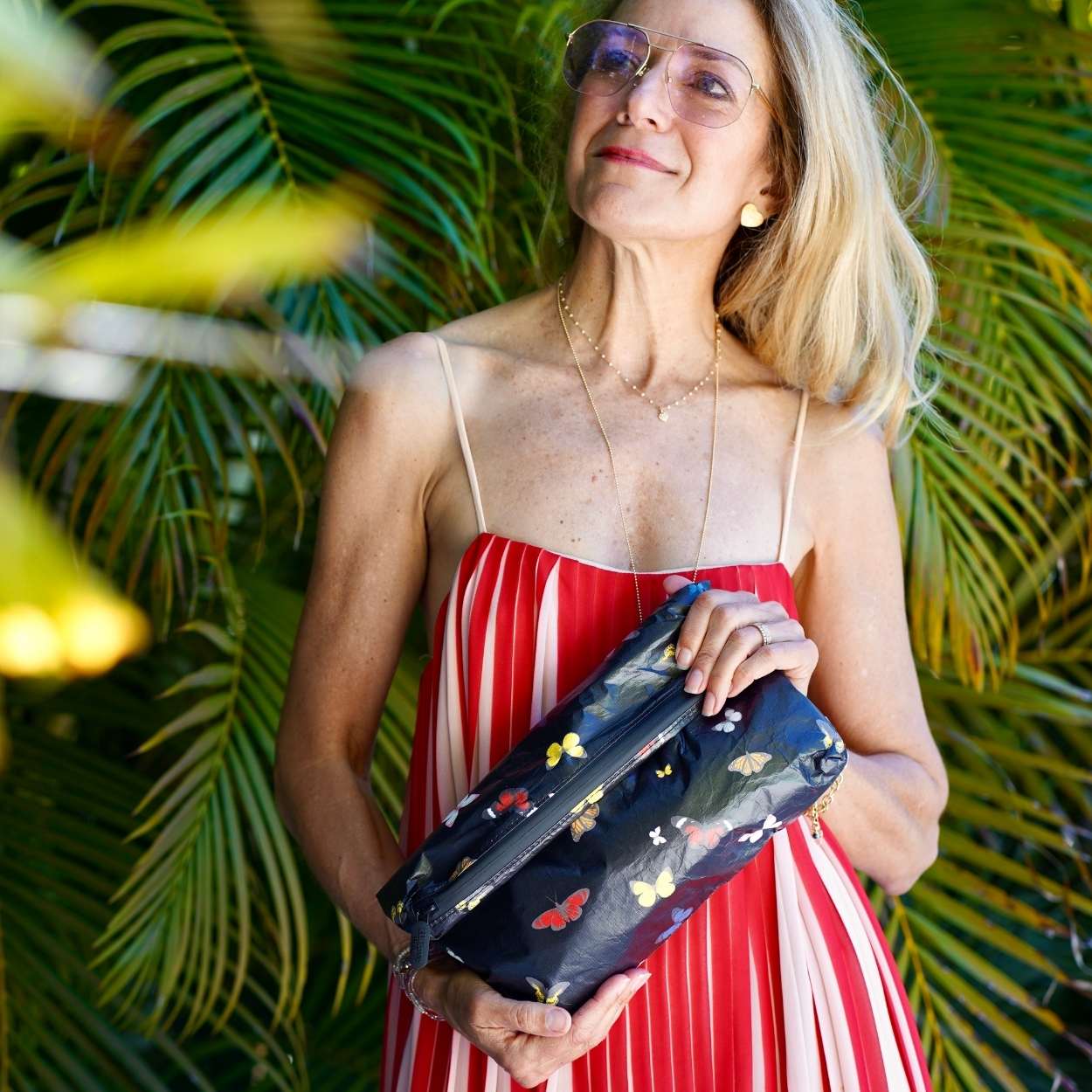 Woman holding a black clutch with butterfly patterns against a green leafy background
