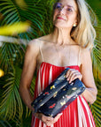Woman holding a black clutch with butterfly patterns against a green leafy background