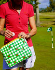 Person on a golf course holding a green bag with golf ball pattern and golf ball