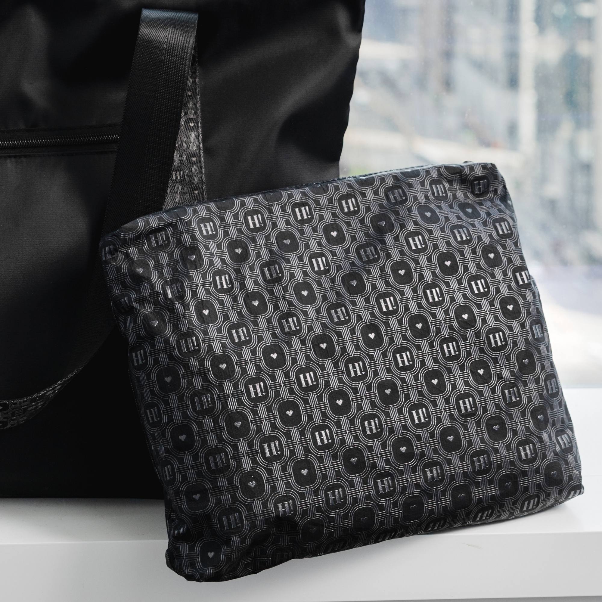 Black signature medium zipper pouch with tonal Hi Love monogram print styled next to a matching black travel bag.