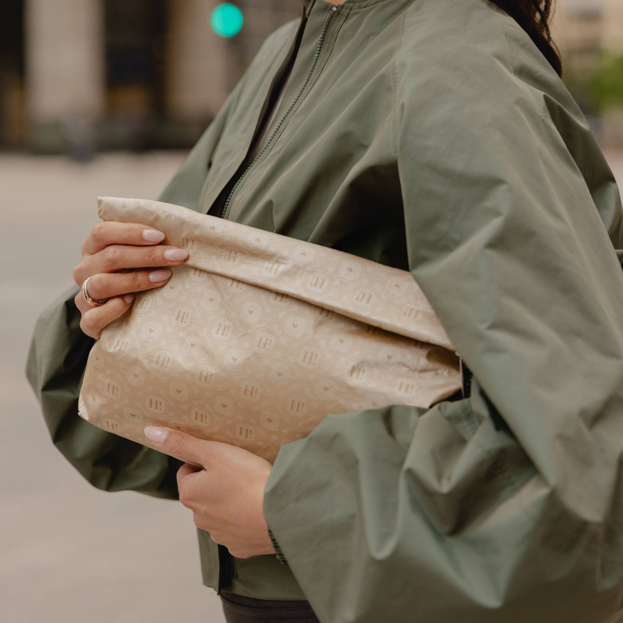 Medium Pouch Signature Shimmer Beige folded as a clutch and held under the arm with a sage green jacket.