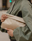 Medium Pouch Signature Shimmer Beige folded as a clutch and held under the arm with a sage green jacket.