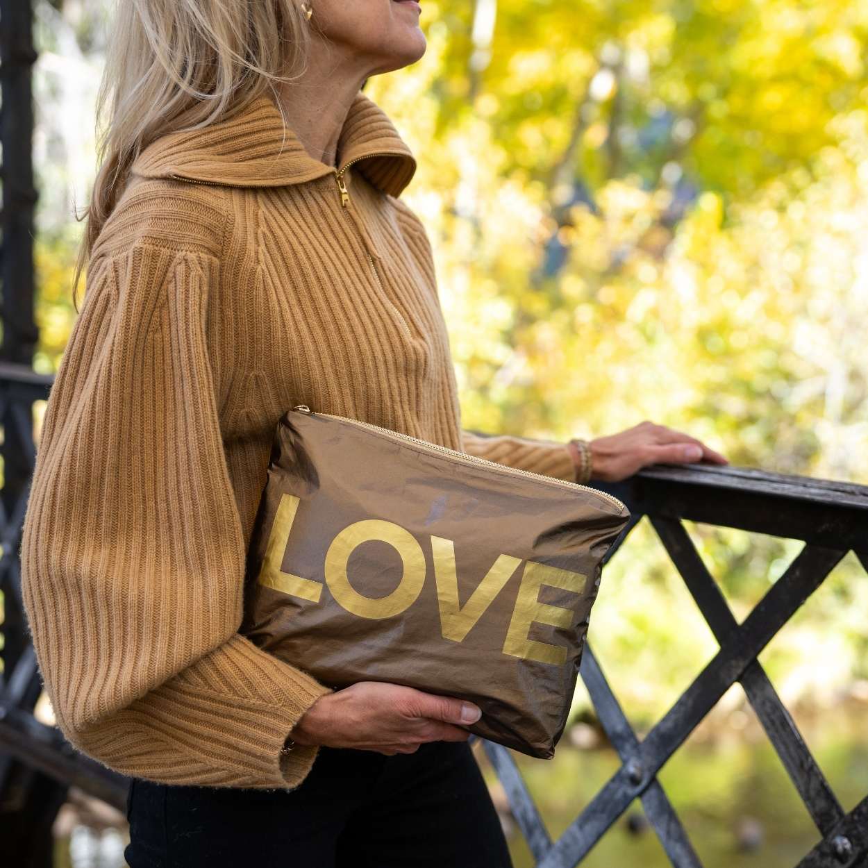 Person standing outdoors holding bronze pouch with gold LOVE printing