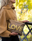 Person standing outdoors holding bronze pouch with gold LOVE printing