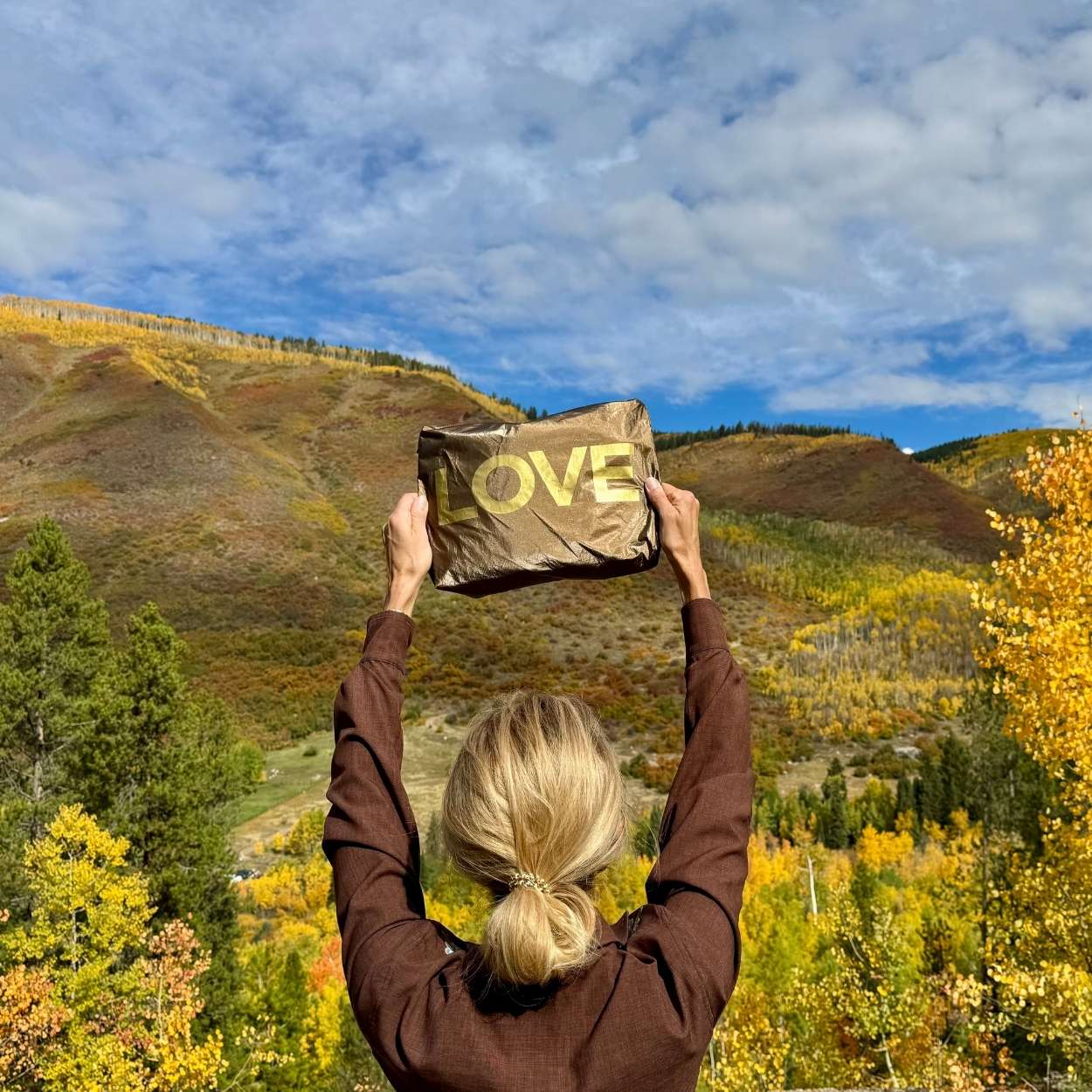 Person standing in a valley with foliage color changes holding bronze pouch with gold LOVE