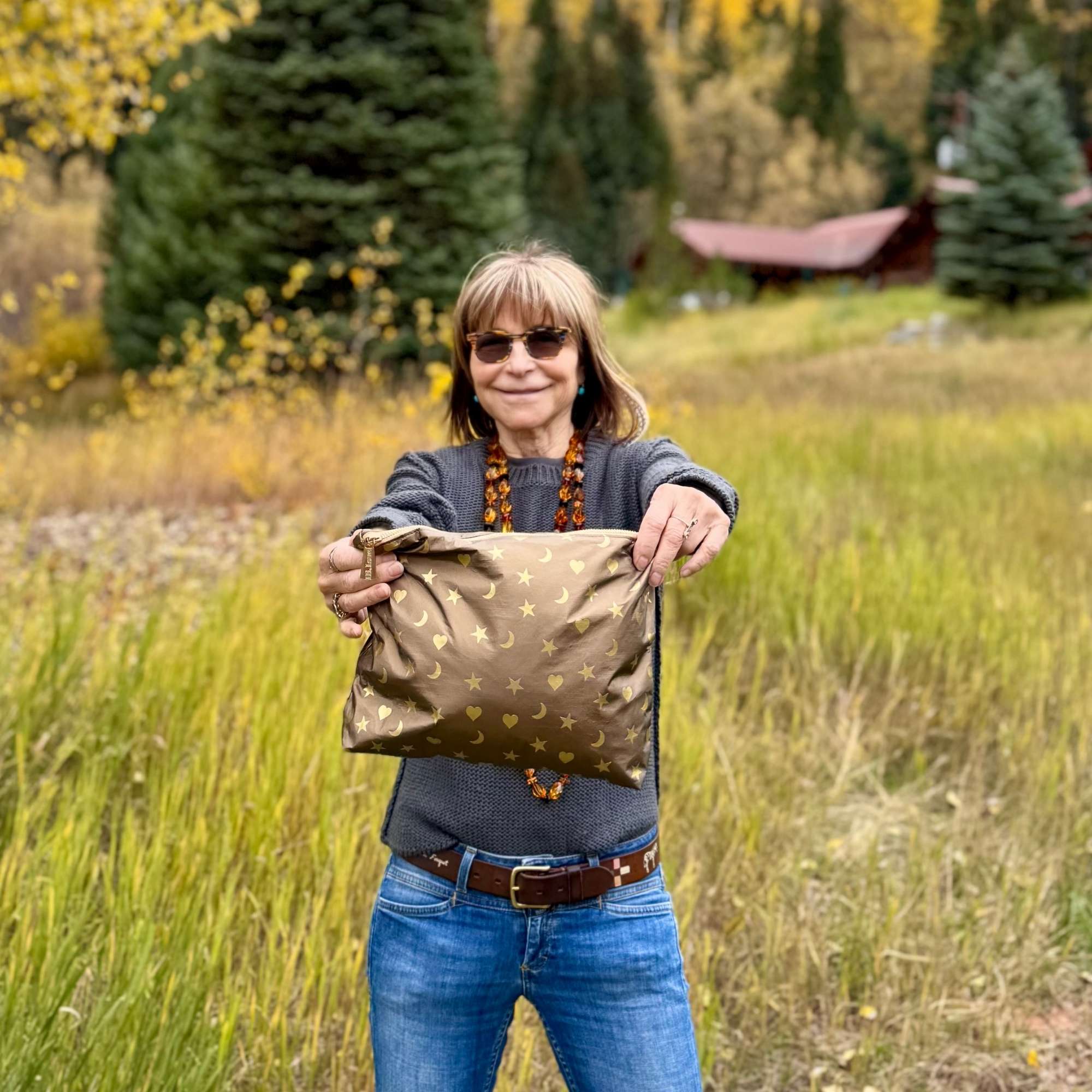Woman holding a Shimmer Bronze Medium Zipper Pouch with metallic gold heart, moon, and star print in a grassy outdoor setting