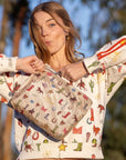 Girl holding a beige pouch with western theme icons printed wearing the coordinating sweatshirt in an outdoor setting.