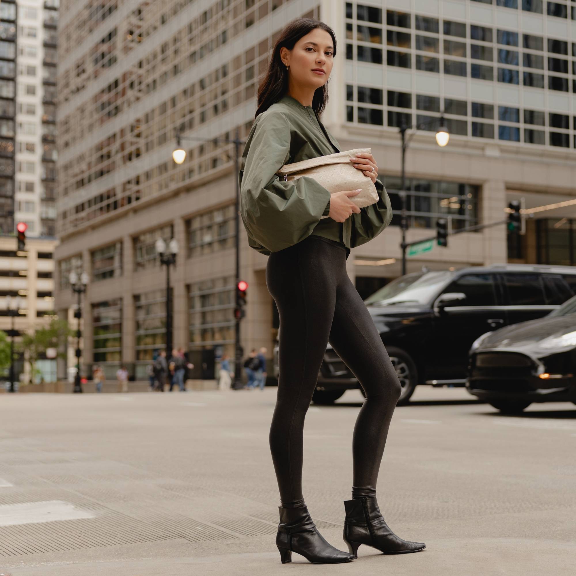 Woman carrying Medium Pouch Signature Shimmer Beige folded as a clutch while standing on a city street.