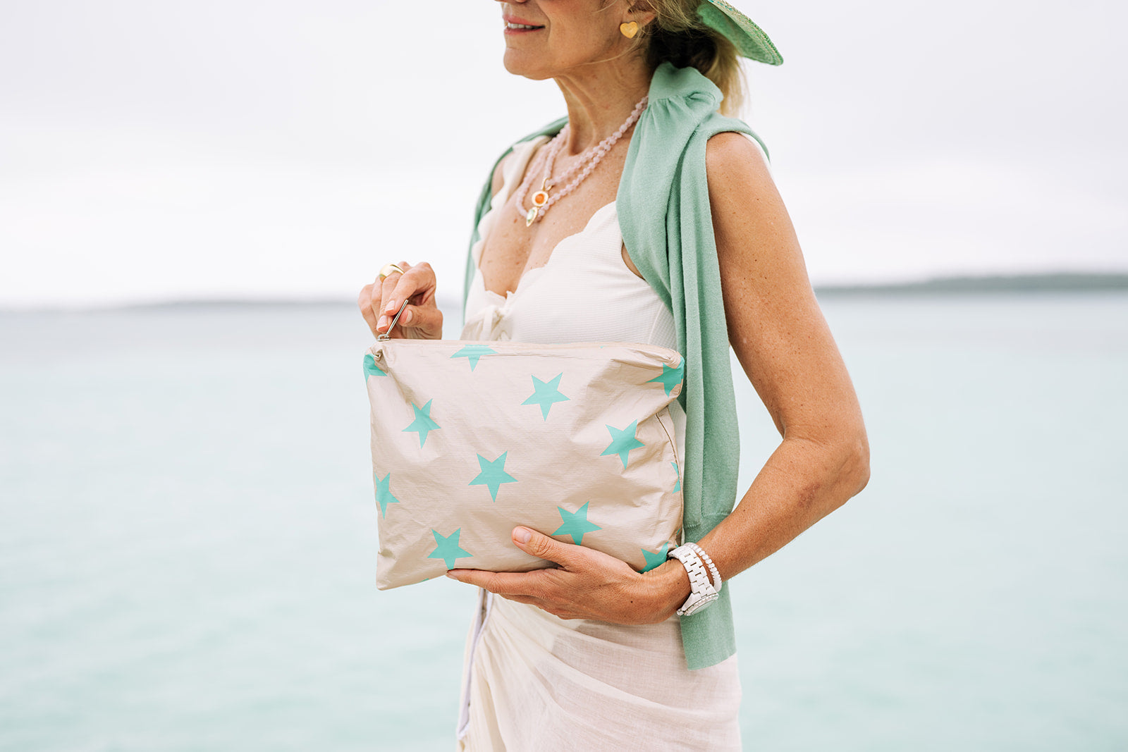 Woman standing by the ocean with a beige and green stars clutch bag