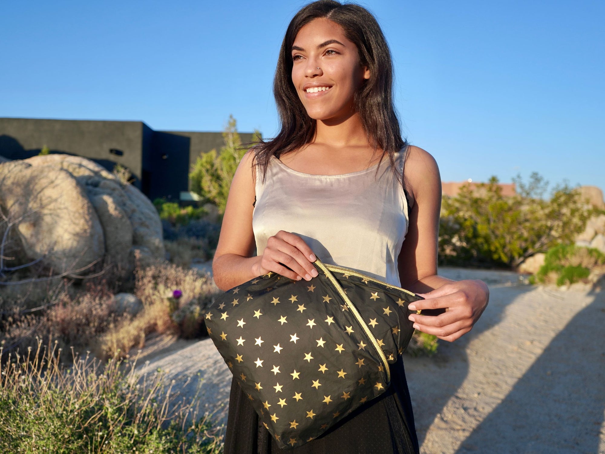 Women with tan silk top and black skirt using a black zipper pouch with gold stars 