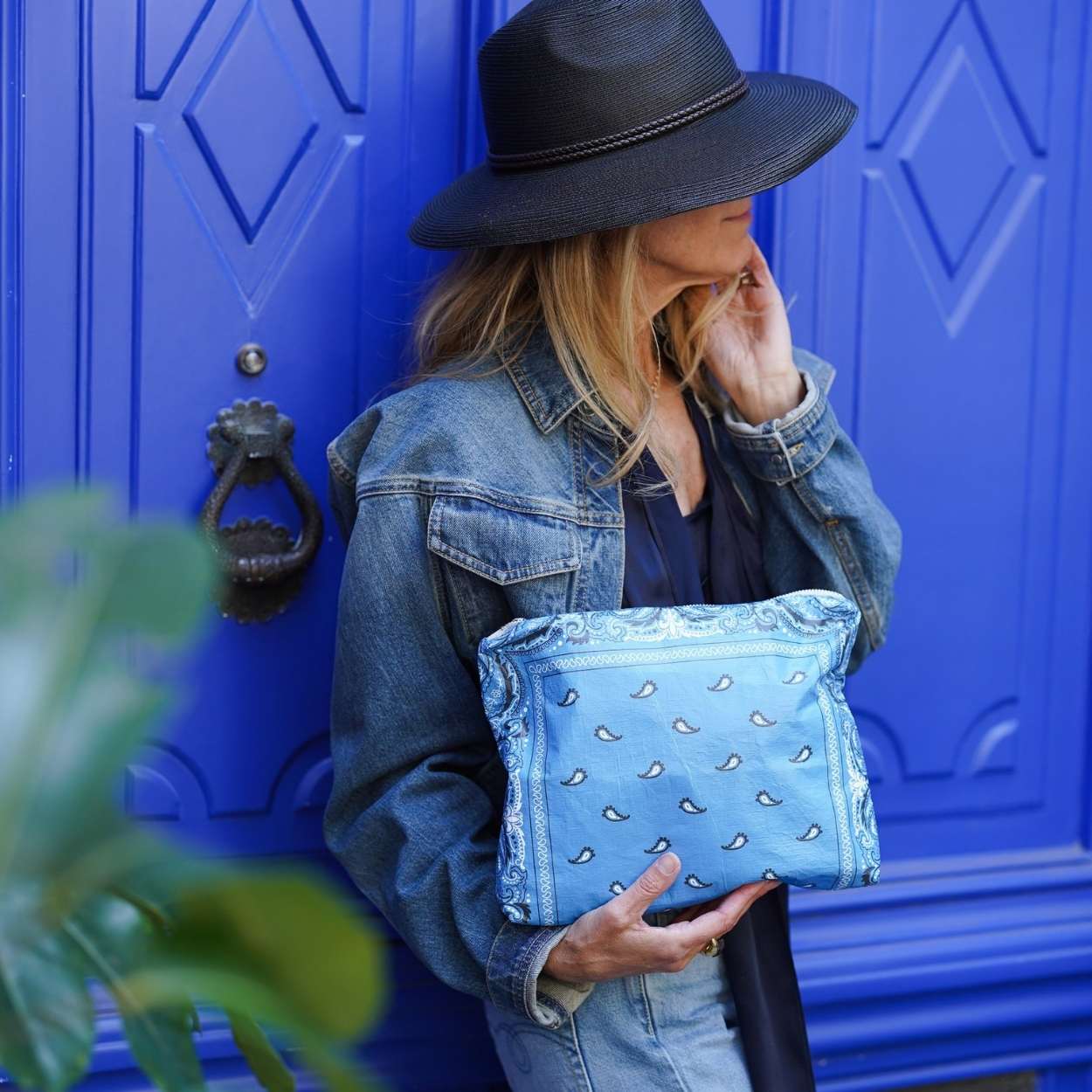 Woman holding a blue bandana clutch in front of a blue door.