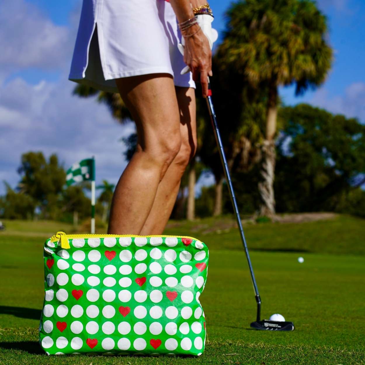 Person on a golf course with a green bag with golf ball pattern, golf club, and ball.